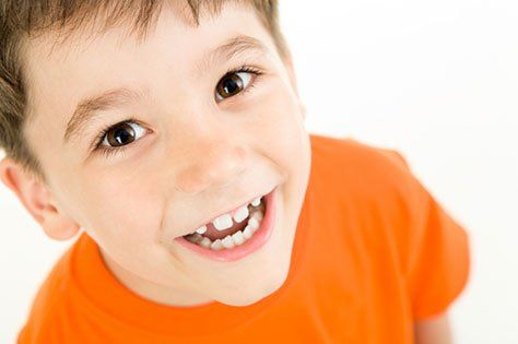 A young boy in an orange shirt is smiling and looking up at the camera.