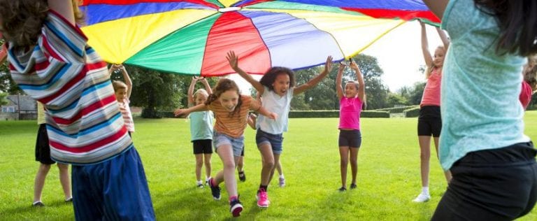 A group of children are playing with a colorful parachute in a park.
