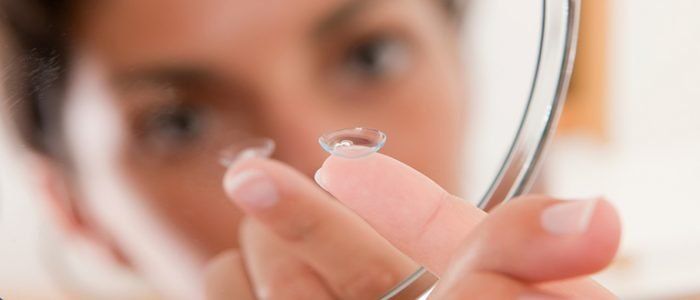 A woman is looking at her contact lenses in a mirror.