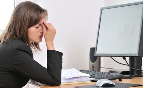 A woman is sitting at a desk with her head in her hands in front of a computer monitor