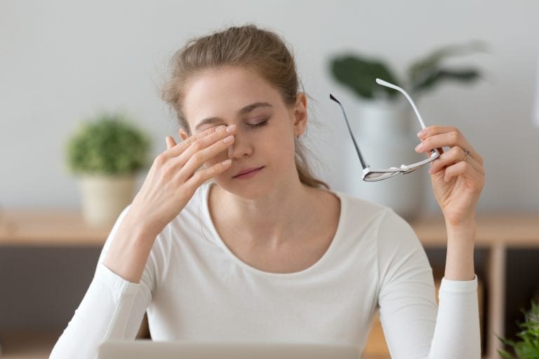A woman is rubbing her eyes while sitting in front of a laptop computer.