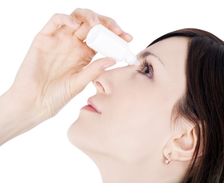 A woman is applying eye drops to her eye