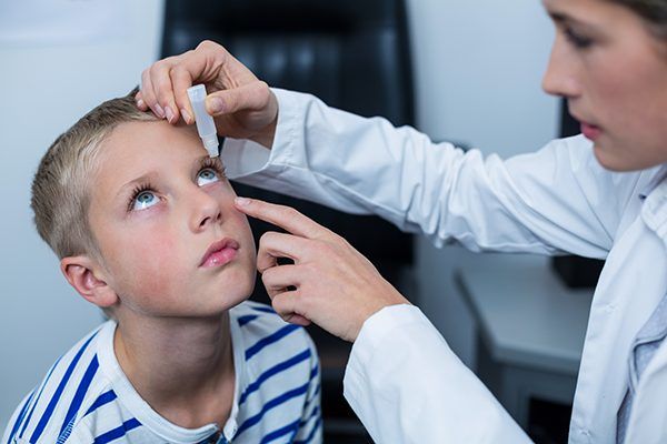 A doctor is applying eye drops to a young boy 's eye.