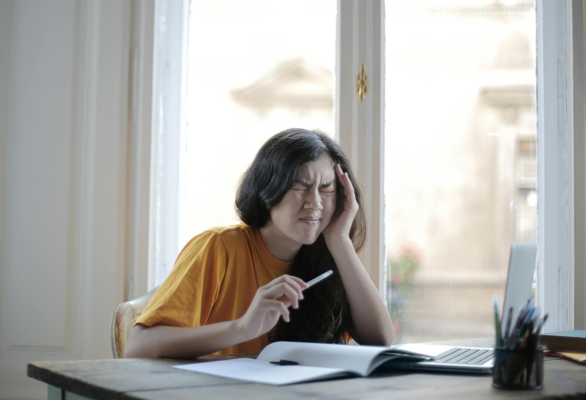 A woman is sitting at a desk with a laptop and a book.