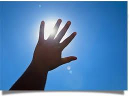 A hand is reaching out towards the sun against a blue sky.