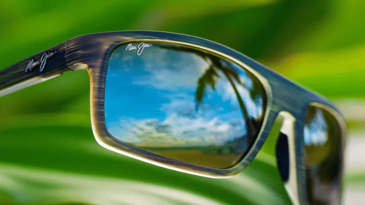 A pair of sunglasses with a reflection of a palm tree in the lenses.