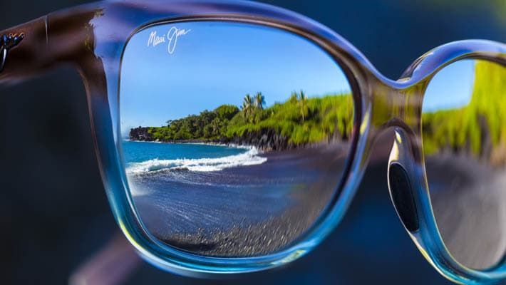 A pair of sunglasses with a reflection of a beach in the lenses.