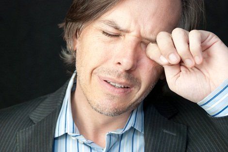 A man in a suit and striped shirt is rubbing his eyes.
