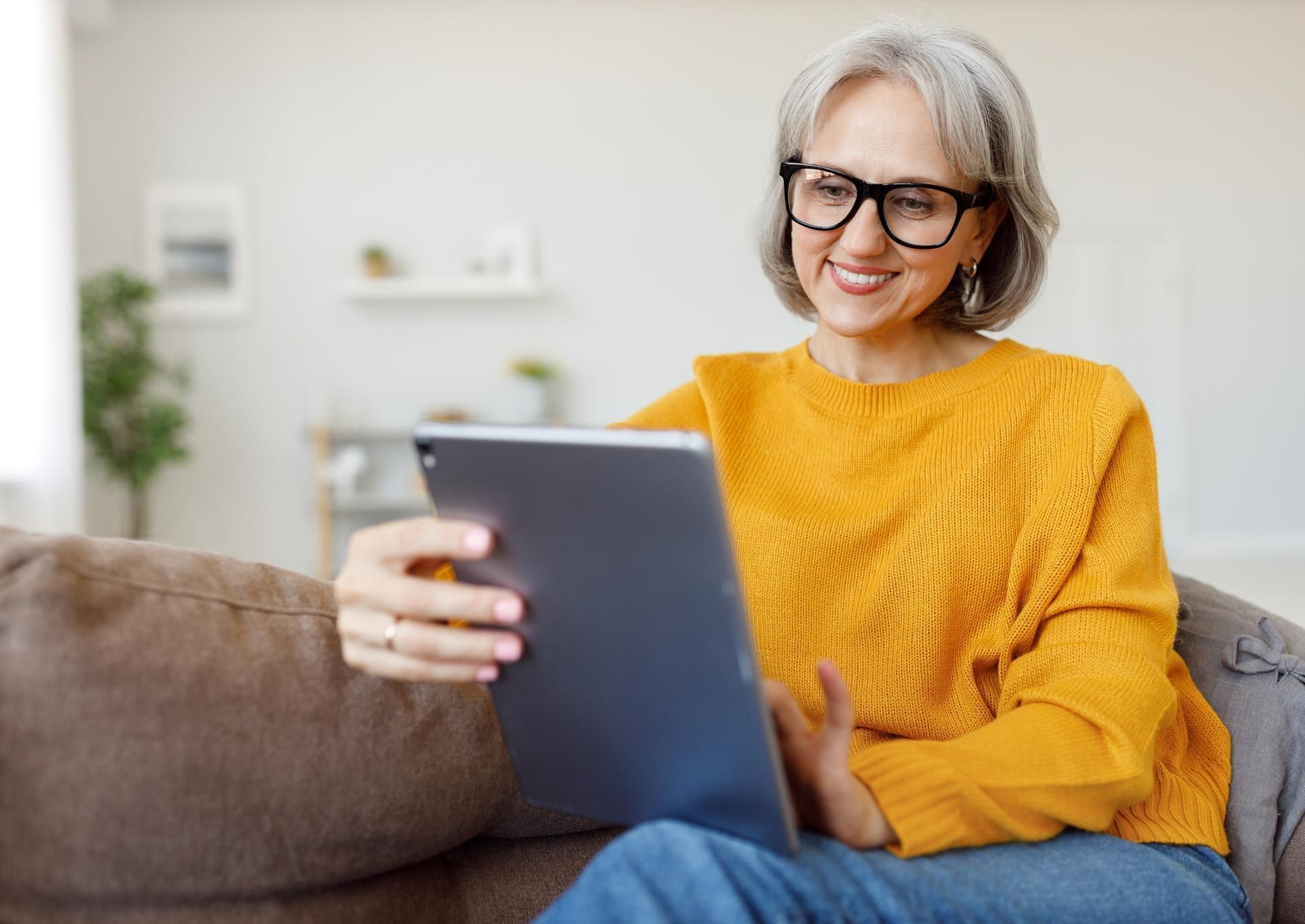 A woman is sitting on a couch using a tablet computer.