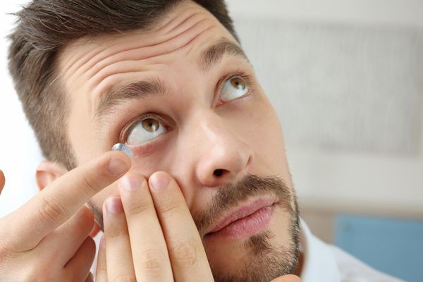 A man is putting a contact lens in his eye.