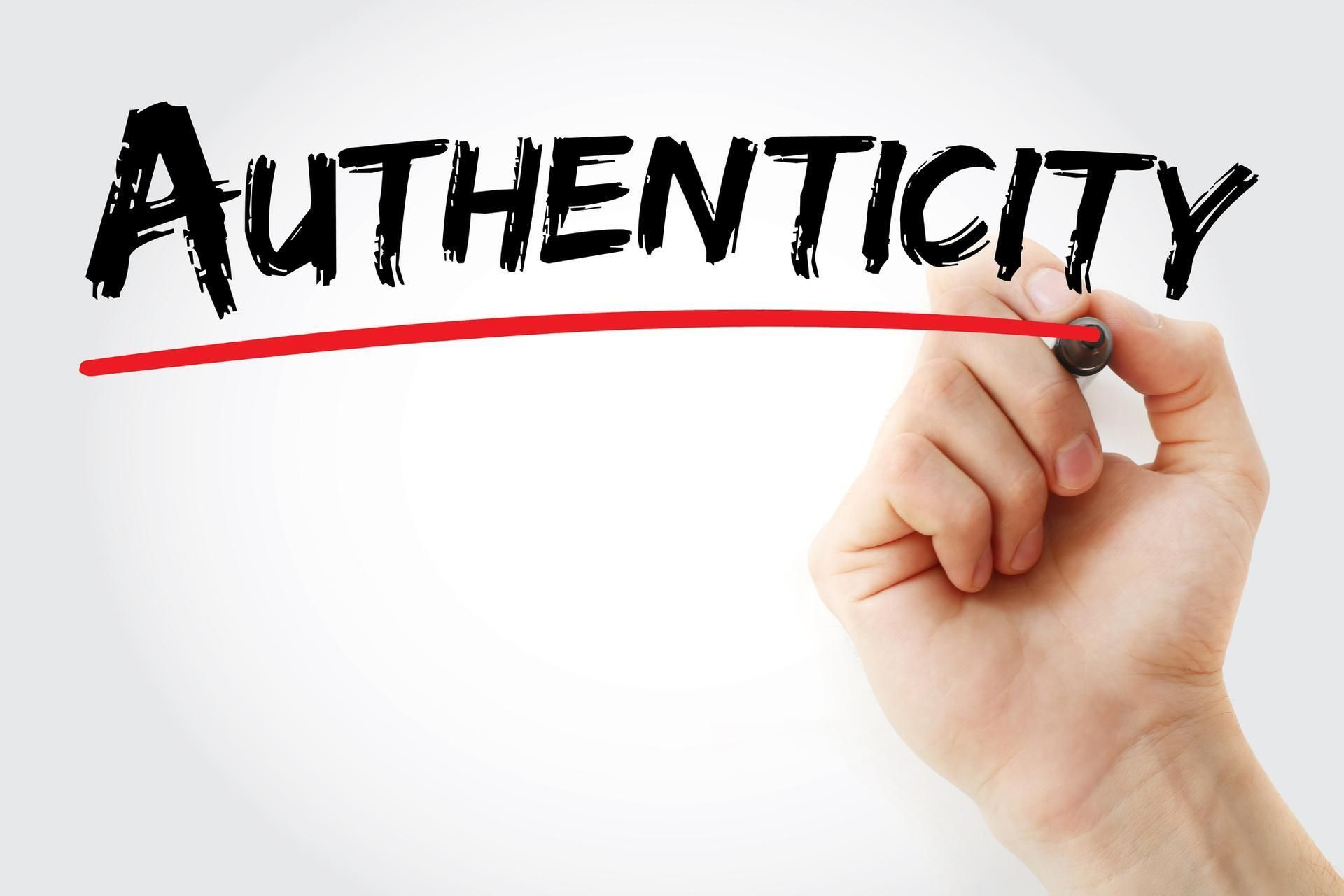 A hand is writing the word authenticity with a marker