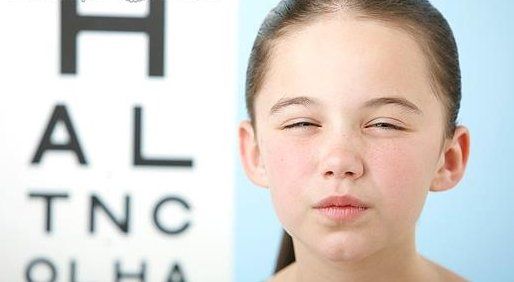 A young girl with her eyes closed in front of an eye chart
