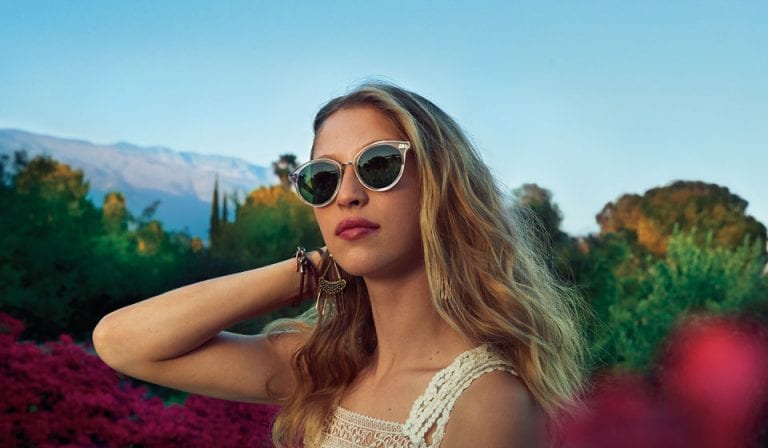 A woman wearing sunglasses is standing in a field of flowers.