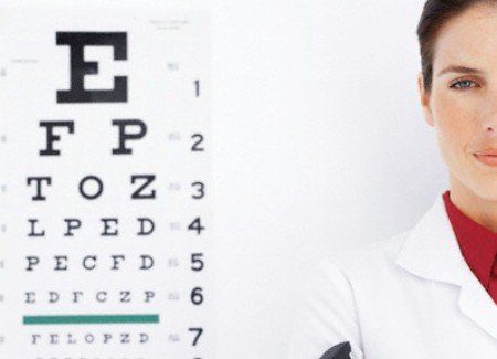 A woman in a lab coat stands in front of an eye chart