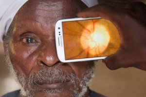 A man is holding a cell phone over his eye.
