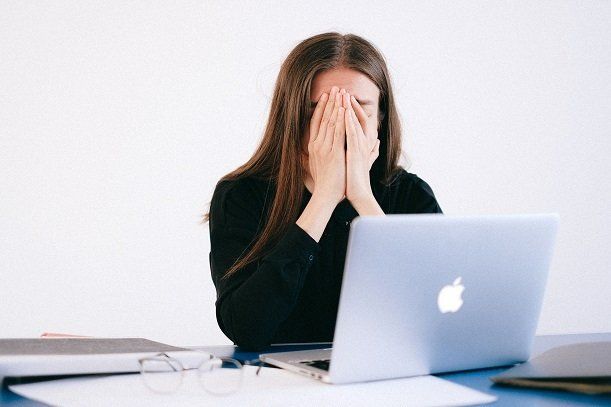 A woman is covering her face while using a laptop computer.