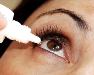 A woman is applying eye drops to her eye