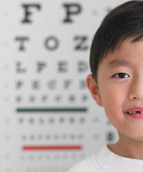 A young boy is standing in front of an eye chart.