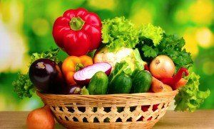 A basket filled with vegetables is sitting on a wooden table.