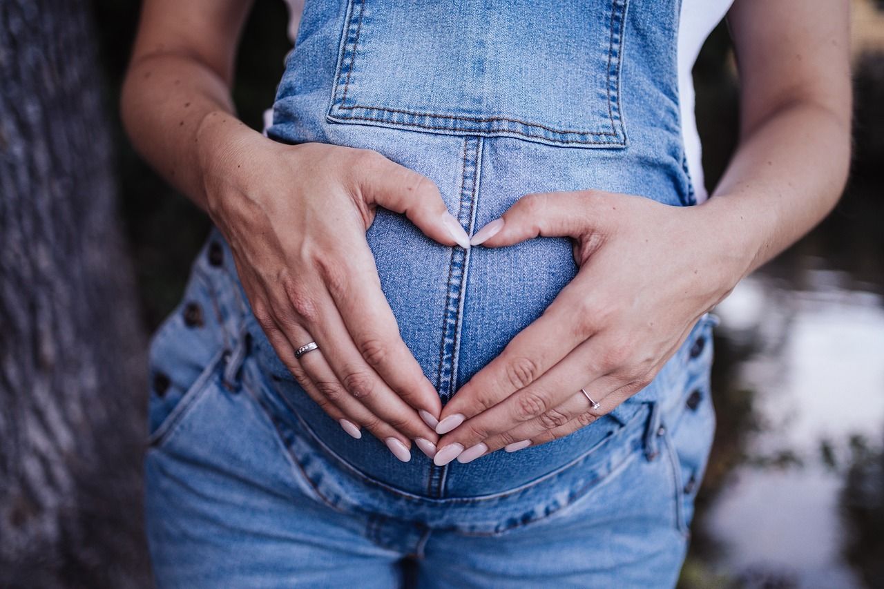 A pregnant woman is making a heart shape with her hands on her belly.