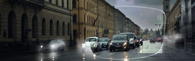 A busy city street with cars driving down it in the rain.