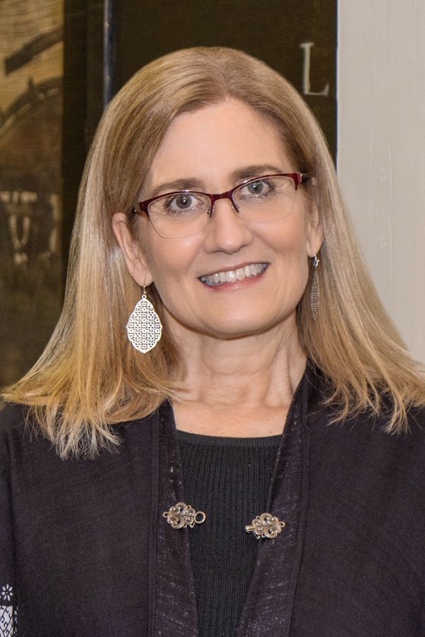 A woman wearing glasses and earrings is smiling for the camera.