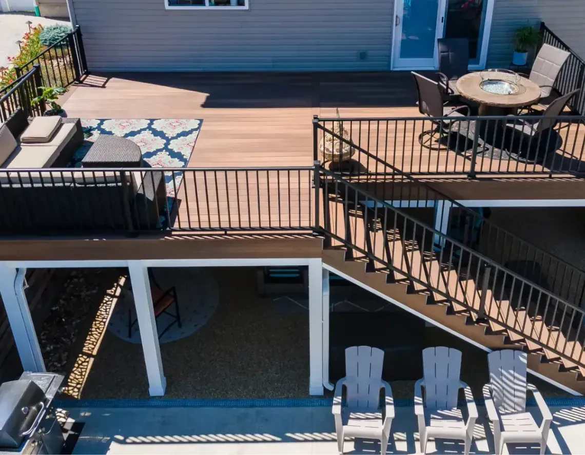 Raised deck with black railings, outdoor seating, and stairs leading to a lower patio with lounge chairs.