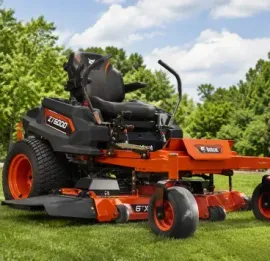 Orange-and-black riding lawn mower on green grass in a sunny yard