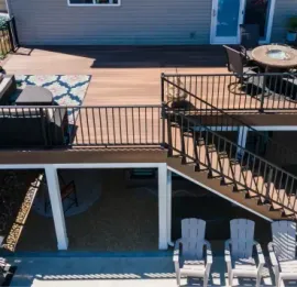 Raised wooden deck with black railings, stairs, and patio furniture behind a house