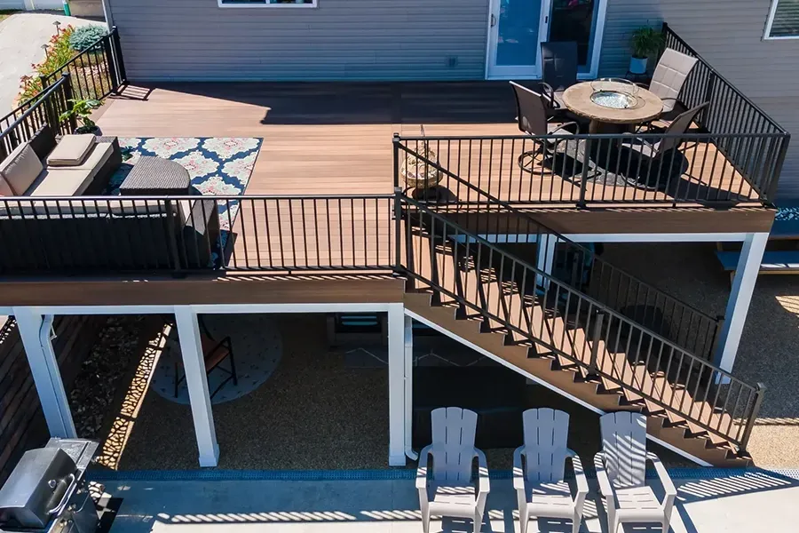 Outdoor deck with black railings, tan seating, and stairs leading to a lower patio with lounge chairs