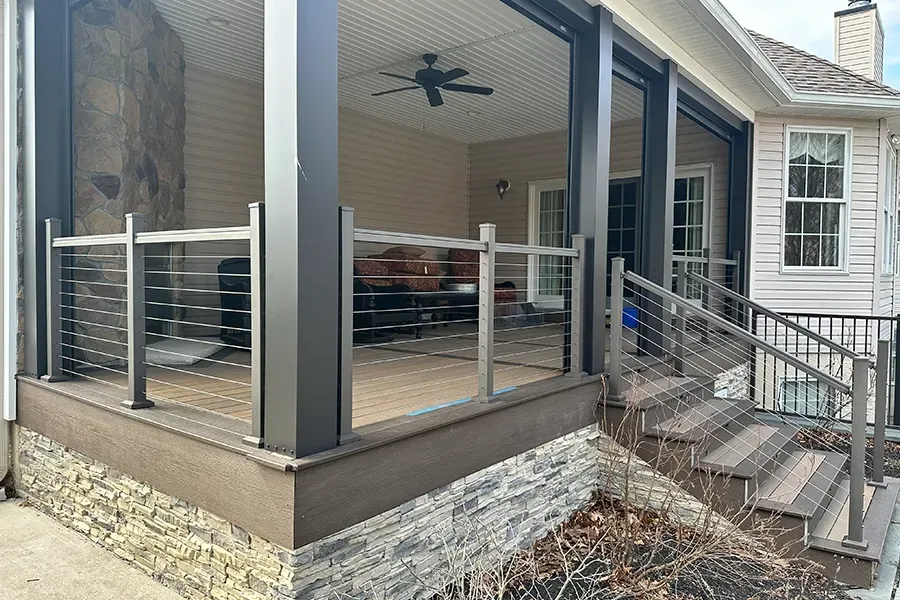 Covered patio with glass railing, ceiling fan, and steps leading down to a backyard.