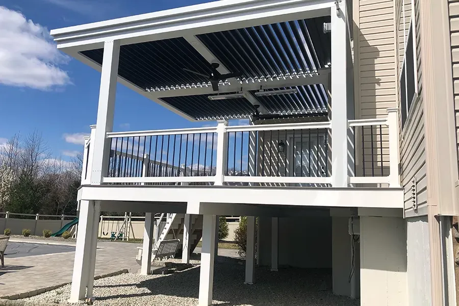 Covered outdoor deck with white railings and steps beneath a pergola, beside a beige house.