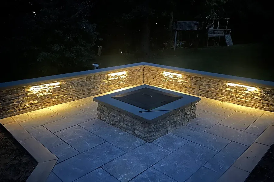 Backyard patio with a lit stone fire pit at night