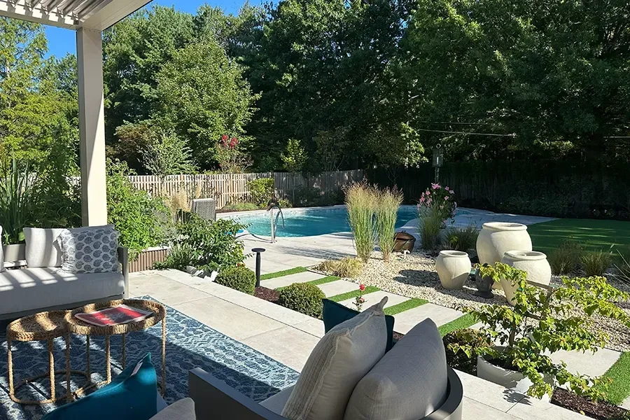 Backyard patio with lounge chairs, pool, and lush green landscaping in bright sunlight