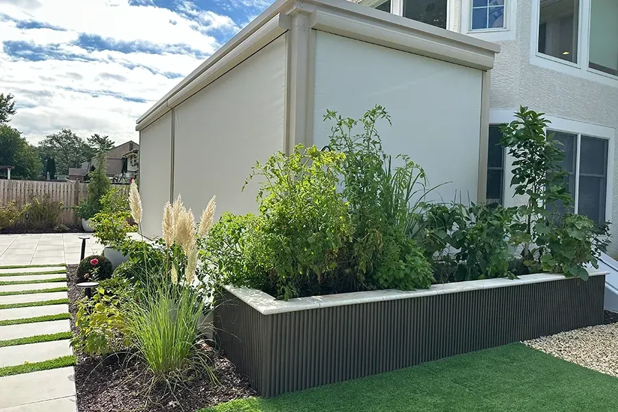 Modern house with raised planter bed, green landscaping, and a paved path along the side yard
