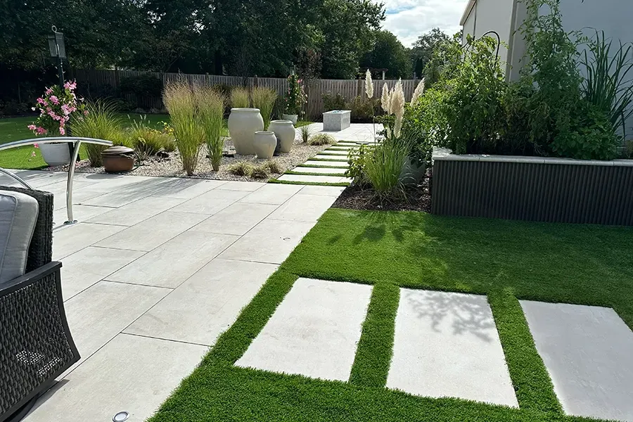 Modern backyard patio with stone pavers, green lawn, and landscaped garden seating area
