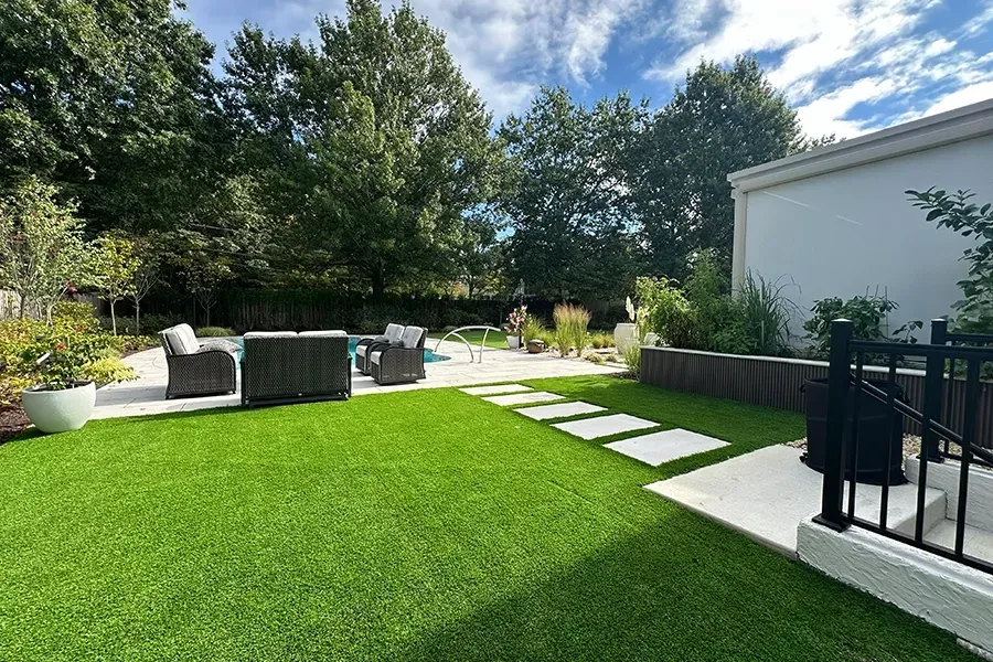 Backyard patio with green lawn, stone path, black furniture, and trees under a bright sky