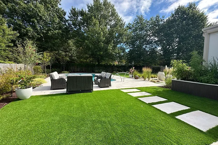 Modern backyard patio with white pavers, green lawn, and outdoor seating under trees
