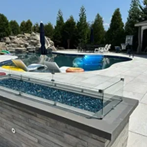 Modern backyard pool with glass fire feature, lounge chairs, umbrella, and inflatables on the water
