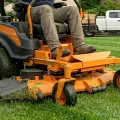 Orange riding lawn mower on grass, with a person seated at the controls.