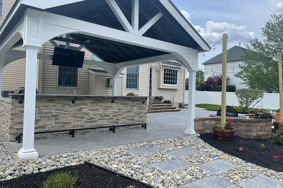 Covered backyard patio with stone bar, black awning, white posts, and gravel landscaping