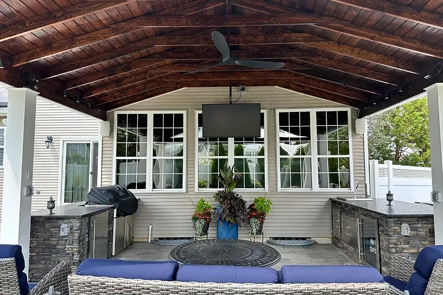 Covered front porch with wooden ceiling, blue cushions, potted flowers, and a ceiling fan