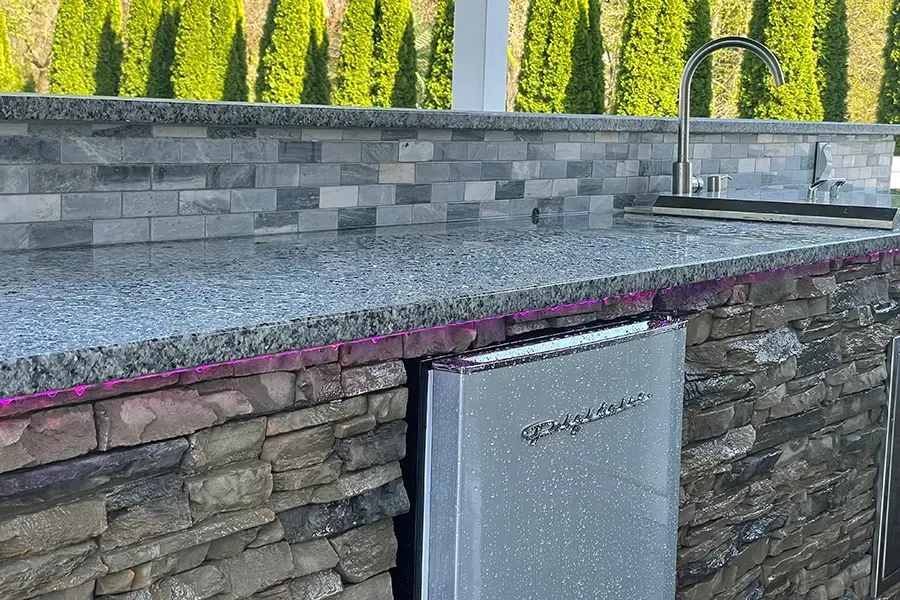 Stone outdoor kitchen counter with built-in stainless cabinet and stacked stone base.