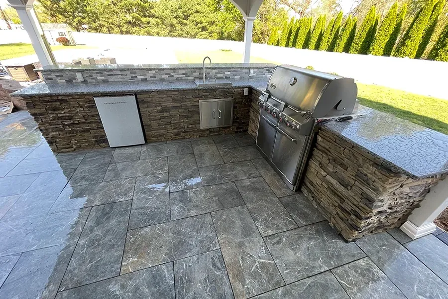Outdoor stone patio with built-in grill, countertop, and sink under a covered pergola