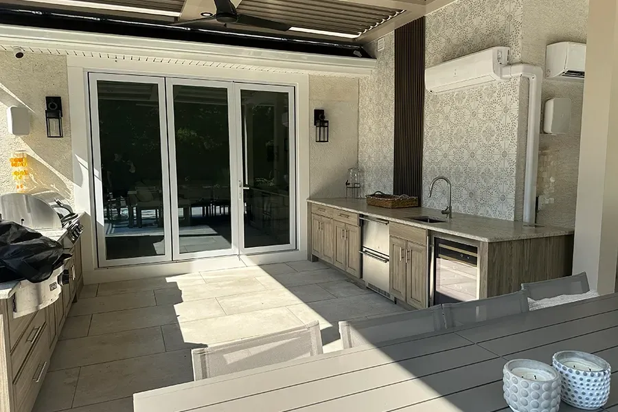 Covered patio with double glass doors, outdoor kitchen, and dining table in bright sunlight