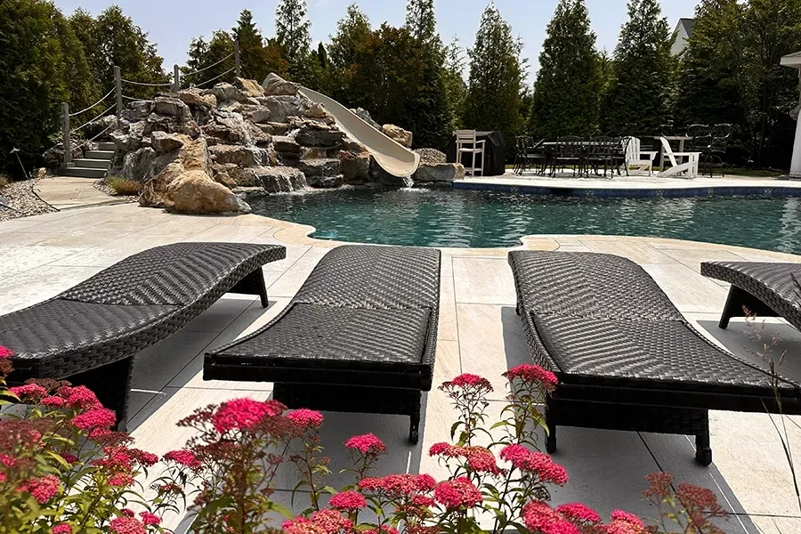Poolside lounge chairs beside a rock waterfall and swimming pool, with flowers in the foreground