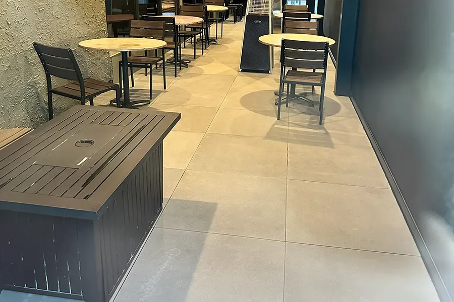 Outdoor café seating area with round tables, chairs, and a wooden bench along a tiled walkway