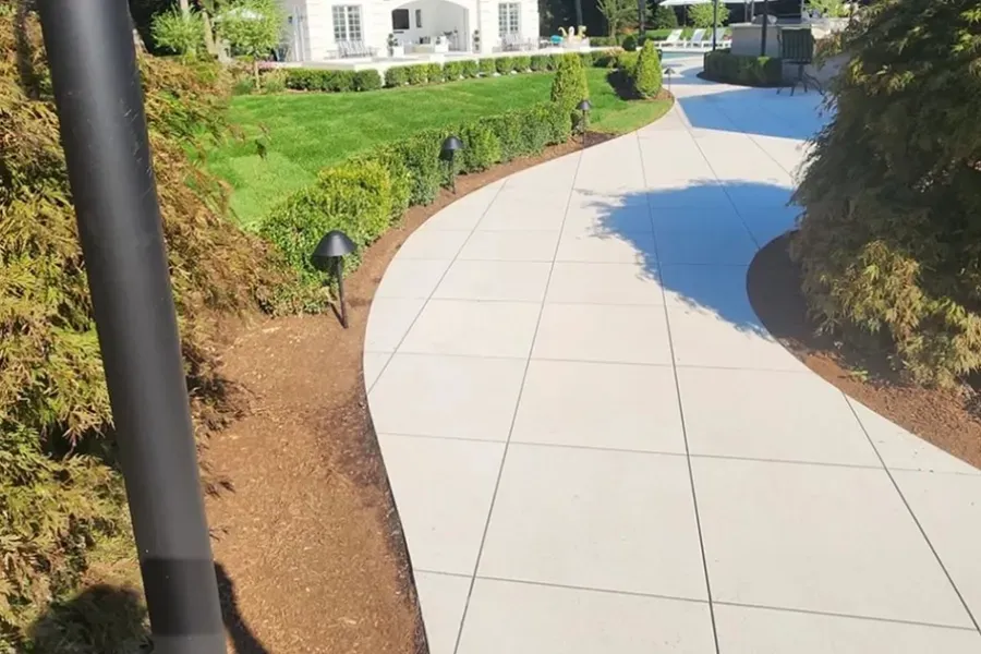 Curved white walkway through landscaped garden with green hedges and small black path lights