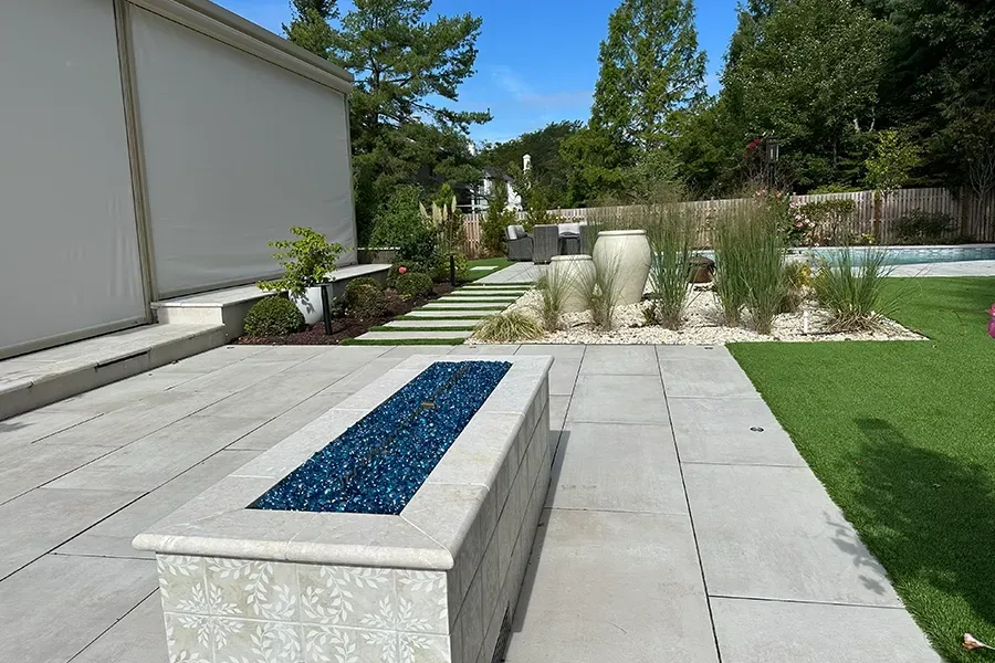 Modern backyard patio with stone benches, steps, gravel planting bed, and lawn under clear skies