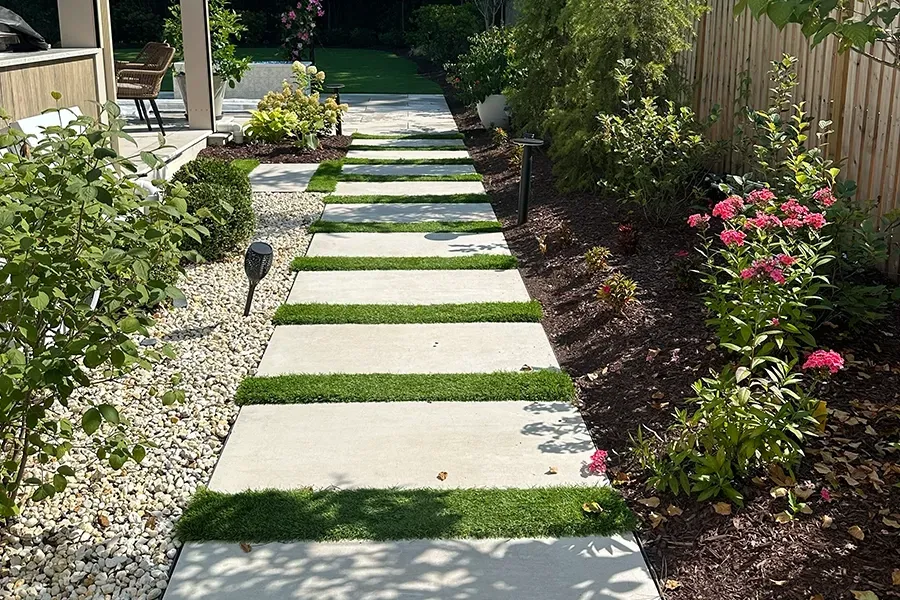 Modern garden path with stepping stones, gravel borders, and flowering shrubs along a fenced walkway